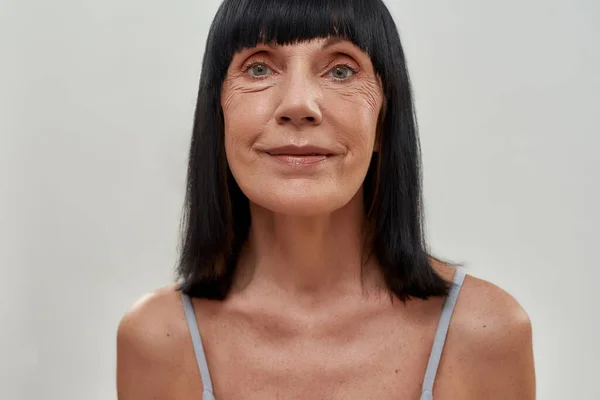 Retrato de una atractiva mujer caucásica de mediana edad mirando a la cámara mientras está de pie sobre un fondo gris, plano vertical — Foto de Stock