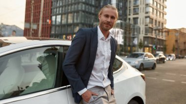 Şehir caddesinde arabanın yanında duran mutlu genç adam.