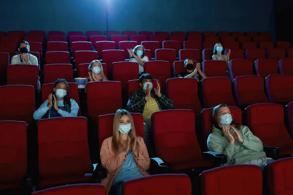 People wearing protective face masks while watching movie in cinema auditorium — Stock Photo, Image