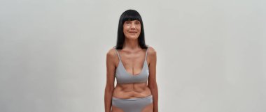 Gri arka planda panoramik pankartta kameraya gülümseyen iç çamaşırlı çekici orta yaşlı beyaz kadın.