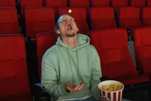 Young guy catching popcorn with his mouth while watching a movie in the cinema alone