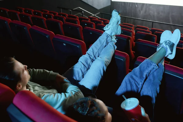 Вид под высоким углом на пару друзей в повседневной одежде, которые кладут ноги на сиденья во время просмотра фильма вместе в пустой аудитории кинотеатра — стоковое фото