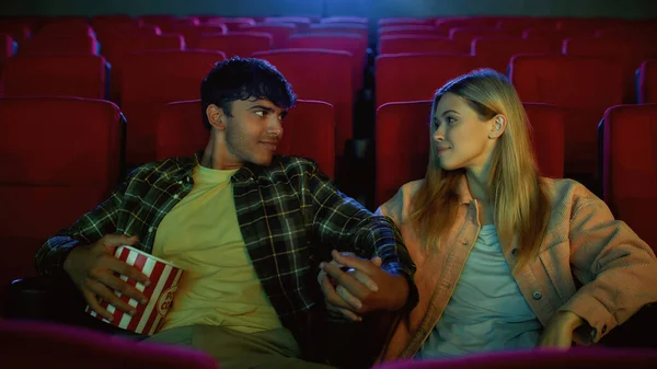 Attractive couple, young man and woman looking at each other while watching movie, sitting at the cinema having romantic movie date — Stock Photo, Image