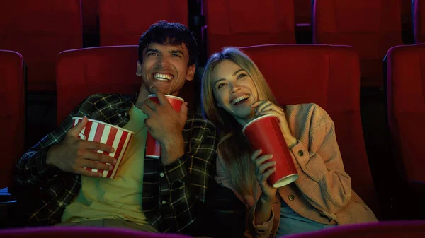 Joyful couple, attractive young man and woman watching movie happily together while sitting at the cinema with popcorn and soda — Stock Photo, Image