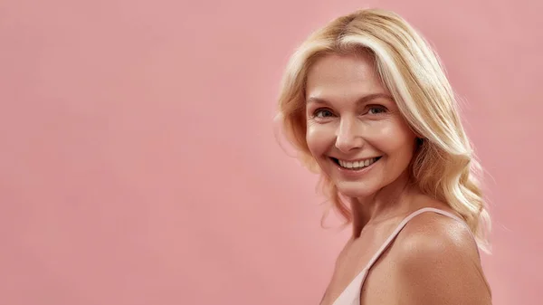 Belleza natural. Retrato de una encantadora mujer rubia madura sonriendo a la cámara, aislada sobre fondo rosa, espacio para copiar texto — Foto de Stock