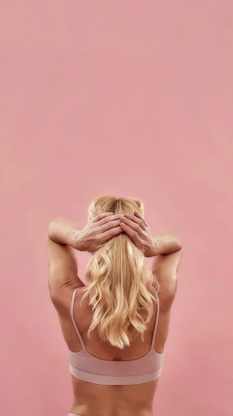 一个半裸的金发女人在粉红背景的工作室摆出美丽而健康的头发的垂直照片 — 图库照片