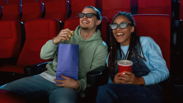 Joyeux jeune couple portant des lunettes 3D riant, tout en regardant un film ensemble dans l'auditorium du cinéma, manger du pop-corn et boire de la soude — Photo