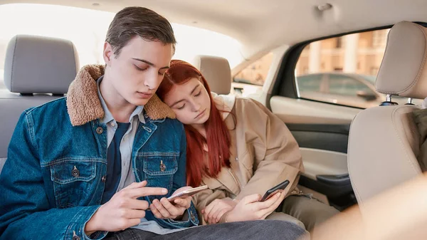Ένα ζευγάρι των εφήβων που αναζητούν κουρασμένος, χρησιμοποιώντας smartphones τους, ενώ κάθονται μαζί στο πίσω κάθισμα στο αυτοκίνητο — Φωτογραφία Αρχείου