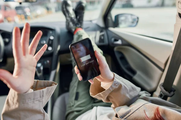 Κοντινό πλάνο της έφηβης που κρατάει smartphone στα χέρια της, κάθεται στο αυτοκίνητο. Ειδοποίηση χαμηλής μπαταρίας στην οθόνη. Η έννοια του εθισμού smartphone — Φωτογραφία Αρχείου