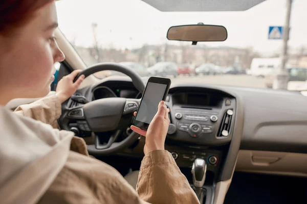 Αποσπάστηκε νεαρή γυναίκα οδηγός κοιτάζοντας την οθόνη του κινητού τηλεφώνου της, ενώ οδηγούσε ένα αυτοκίνητο. Έννοια τεχνολογίας και μεταφορών — Φωτογραφία Αρχείου