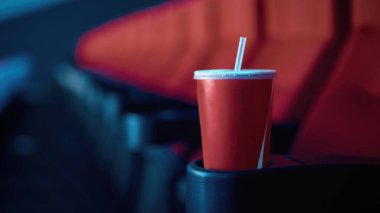 Arka planda kırmızı sinema koltukları olan boş bir soda bardağına odaklan.