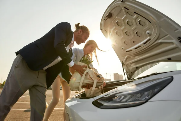 Vrolijke jonge man en vrouw zetten tassen in het voertuig — Stockfoto
