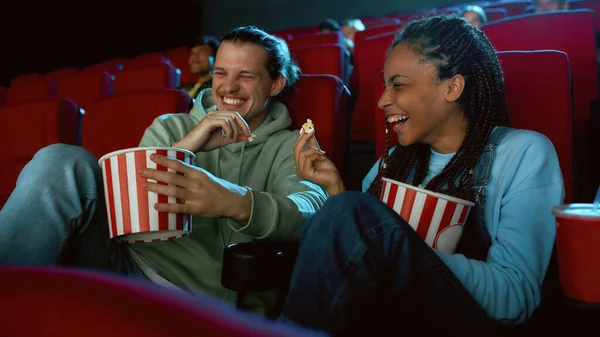 Gut gelaunte beste Freunde, die lachen, Popcorn essen, während sie sich gemeinsam Filme ansehen, im Kinosaal sitzen — Stockfoto