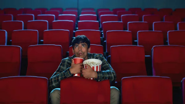 Focused handsome young man holding a drink and popcorn basket while watching movie alone in empty theater auditorium — Stock Photo, Image