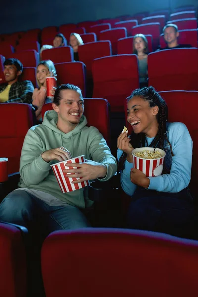 Fröhliches junges Paar, lachend, Popcorn trinkend, während es gemeinsam im Kinosaal sitzt — Stockfoto