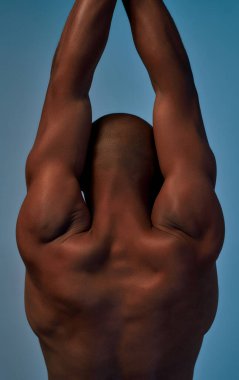 Kollarını kaldırıp sırt kaslarını geren Afro-Amerikalı bir sporcu.