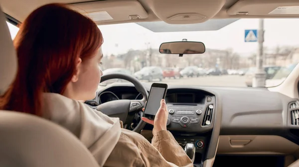 Αποσπάστηκε νεαρή γυναίκα οδηγός κοιτάζοντας την οθόνη του κινητού τηλεφώνου της, ενώ οδηγούσε ένα αυτοκίνητο. Έννοια τεχνολογίας και μεταφορών — Φωτογραφία Αρχείου