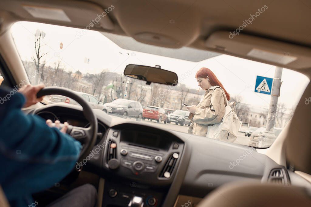 Distracted teenage girl texting, using her mobile phone while crossing the street. Male driver honking the horn in the car. Technology and transportation concept