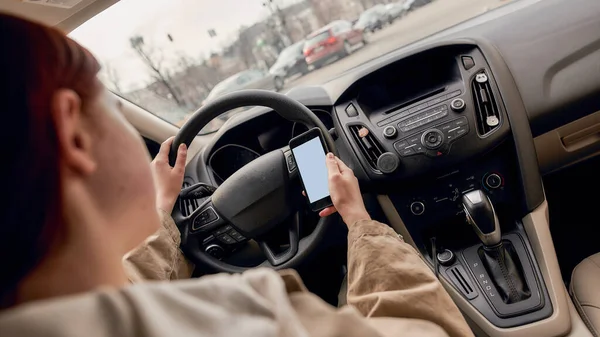 Motorista jovem distraído olhando para a tela de seu telefone celular enquanto dirige um carro. Conceito de tecnologia e transporte — Fotografia de Stock