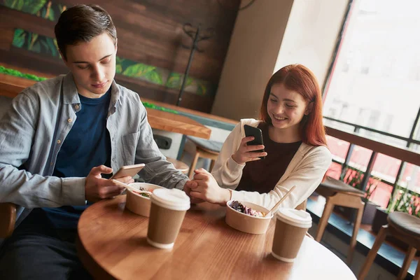 Ένα ζευγάρι εφήβων κρατώντας το χέρι, ενώ τη λήψη φωτογραφιών με το γεύμα τους, χρησιμοποιώντας smartphone, κάθεται σε ένα καφέ μαζί την ημέρα — Φωτογραφία Αρχείου