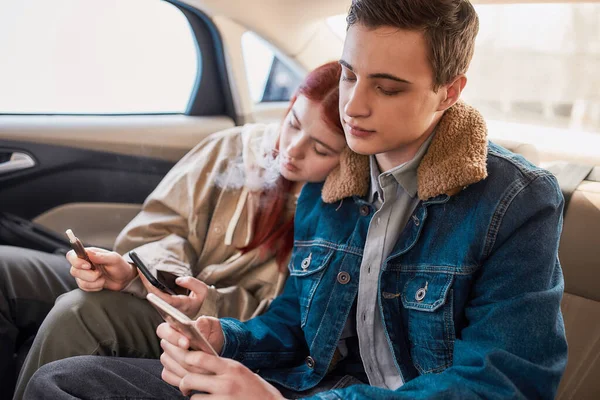 Ένα ζευγάρι των εφήβων απορροφάται εντελώς από τη χρήση των τηλεφώνων τους, αγνοώντας ο ένας τον άλλον, ενώ κάθονται μαζί στο πίσω κάθισμα του αυτοκινήτου — Φωτογραφία Αρχείου