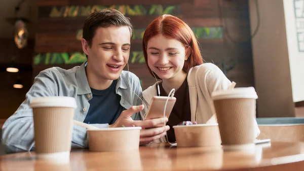 Ευτυχισμένο έφηβο ζευγάρι που δείχνει συναισθηματικό ενώ βλέπει κάτι χρησιμοποιώντας smartphone και ίδια ακουστικά, να κάθονται σε ένα καφέ μαζί την ημέρα — Φωτογραφία Αρχείου