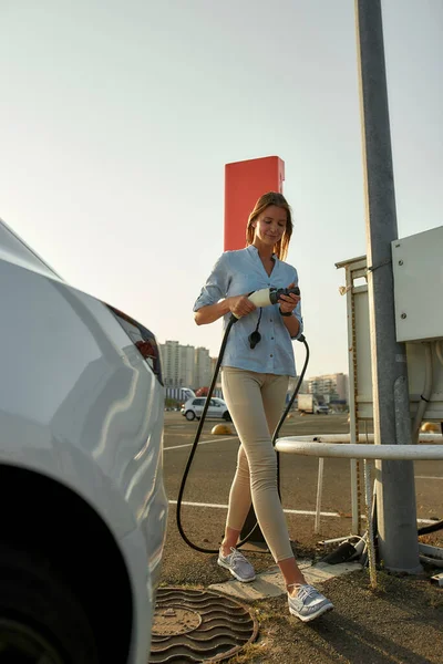 Vrouw neemt autolader van elektrisch oplaadstation — Stockfoto