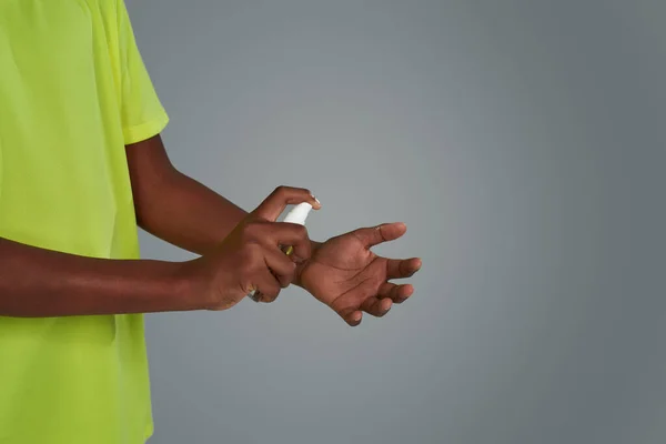 Beskuren bild av afrikansk pojke i neon t-shirt sprutning desinfektionsmedel på händerna medan du står mot grå bakgrund — Stockfoto