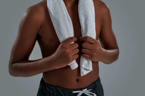 Foto recortada de un chico africano medio desnudo sosteniendo la toalla sobre los hombros, descansando después del entrenamiento mientras está de pie sobre un fondo gris — Foto de Stock