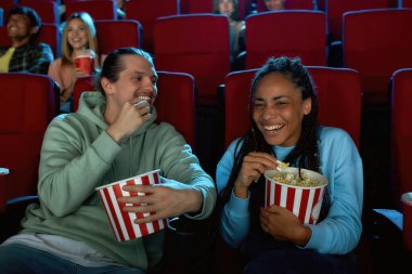 Mutlu genç çift gülüyor, film izlerken patlamış mısır yiyor, sinema salonunda oturuyor.