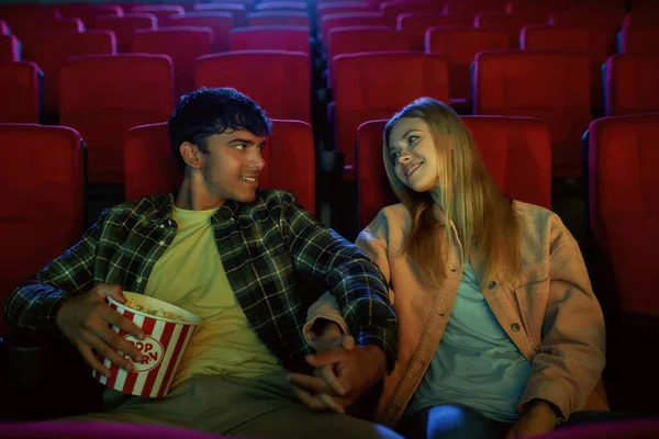 Aantrekkelijk koppel, jonge man en vrouw glimlachend naar elkaar, hand in hand tijdens het kijken naar de film, zitten in de bioscoop met romantische film date — Stockfoto