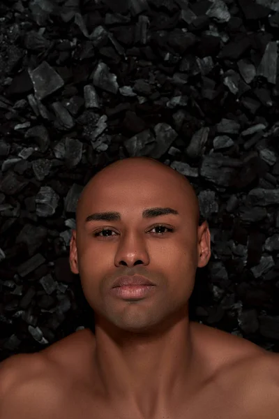Close up retrato de belo jovem afro-americano olhando para a câmera, posando isolado sobre fundo de carvão negro — Fotografia de Stock