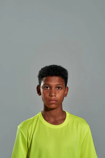 Ritratto di un ragazzo africano adolescente che guarda la macchina fotografica mentre posa isolato su sfondo grigio in studio, scatto verticale — Foto Stock