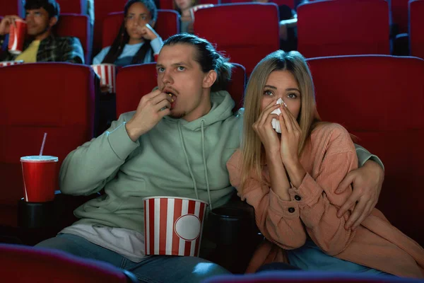 Сосредоточились на молодой паре, выглядящей эмоционально, когда ели попкорн и смотрели кино вместе, сидя в кинозале — стоковое фото
