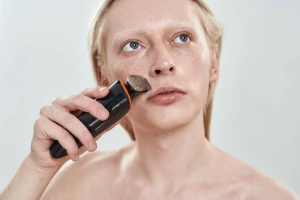 Portrait of young man using trimmer on mustache area — Stock Photo, Image