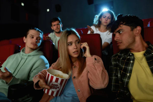 Attraktive junge Frau telefoniert, nerviges Publikum beim Kinobesuch mit Freunden — Stockfoto