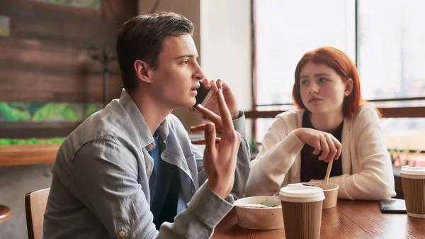 Dos adolescentes pasando tiempo juntos, sentados en un café durante el día. Chica aburrida, comiendo su comida mientras su novio la ignora, hablando por teléfono — Foto de Stock