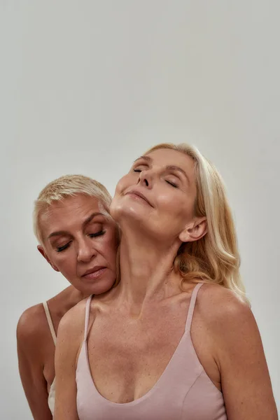 Studio portrait of two sensual blonde women standing together, posing isolated over gray background — Stock Photo, Image