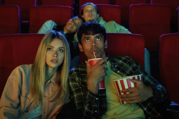 Сосредоточенные молодая пара, привлекательный мужчина и женщина действительно заинтересованы в просмотре фильма, сидя в кинотеатре, едят попкорн и пить кокаин — стоковое фото