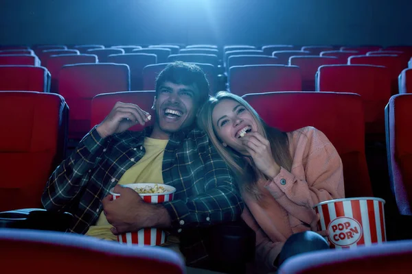Joyeux jeune couple, homme et femme séduisant souriant, assis au cinéma, regardant un film et mangeant du pop-corn — Photo