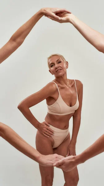 Mulher idosa caucasiana orgulhosa em roupa interior olhando para a câmera enquanto posando semi-nua isolada sobre fundo claro. Mulheres fazendo moldura com os braços — Fotografia de Stock