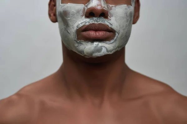 Πρόσωπο closeup του shirtless νεαρός αφροαμερικανός άνδρας χρησιμοποιώντας μάσκα αφαίρεσης του προσώπου μαύρο κεφάλι, θέτουν απομονώνονται πάνω από γκρι φόντο — Φωτογραφία Αρχείου