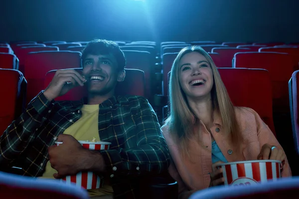 Fröhliches Paar, junge Männer und Frauen, die Spaß haben, im Kino sitzen, einen Film sehen und Popcorn essen — Stockfoto