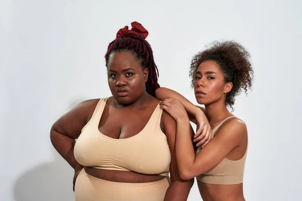 Studio shot of two confident plus size and slim african american female  models in beige underwear looking at camera while posing together isolated  over yellow background Stock Photo by ©LanaStock 468749008