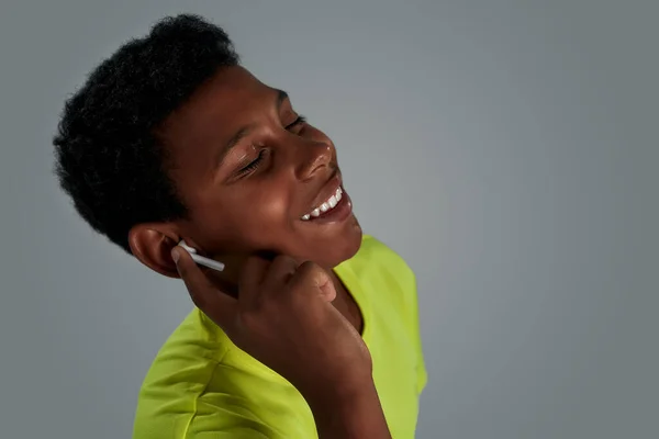 Retrato de um adolescente africano feliz usando fones de ouvido sem fio e sorrindo, mantendo os olhos fechados enquanto ouve música — Fotografia de Stock