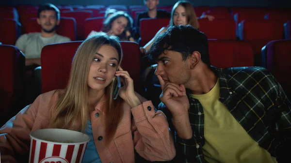 Portret van een aantrekkelijke jonge vrouw praten aan de telefoon, vervelend publiek en haar vriend tijdens het kijken naar de film in de bioscoop, met romantische film date — Stockfoto