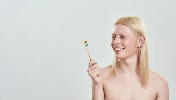 Sonriente joven rubio mirando el cepillo de dientes en la mano —  Fotos de Stock