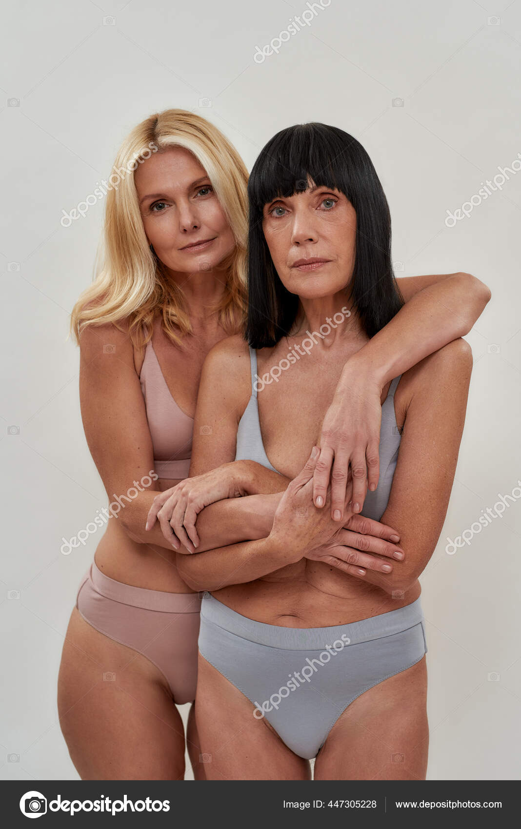 Two beautiful women in underwear looking at camera holding hands, embracing each other while posing together over light background image photo