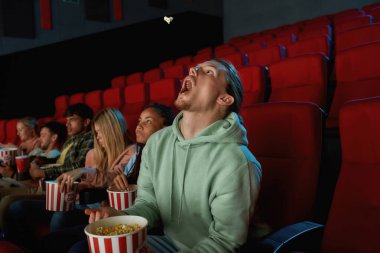 Genç adam arkadaşlarıyla sinemada film izlerken ağzıyla patlamış mısır yakalıyor.