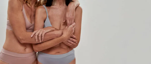 Plan recadré de deux femmes en sous-vêtements, s'embrassant tout en posant ensemble sur un fond clair. Chaleur en relation, concept de beauté mature — Photo